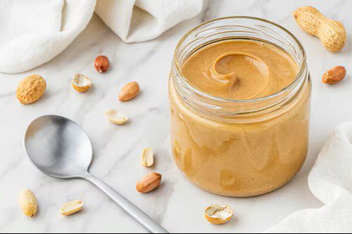 Open peanut butter jar, spoon and shelled peanuts