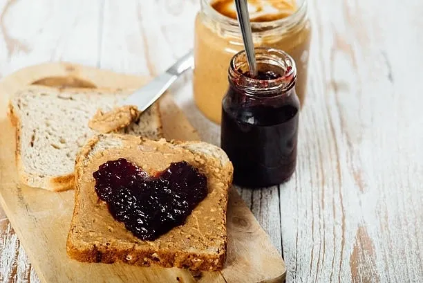 Knife with peanut butter and toast with peanut butter and heart-shaped jam