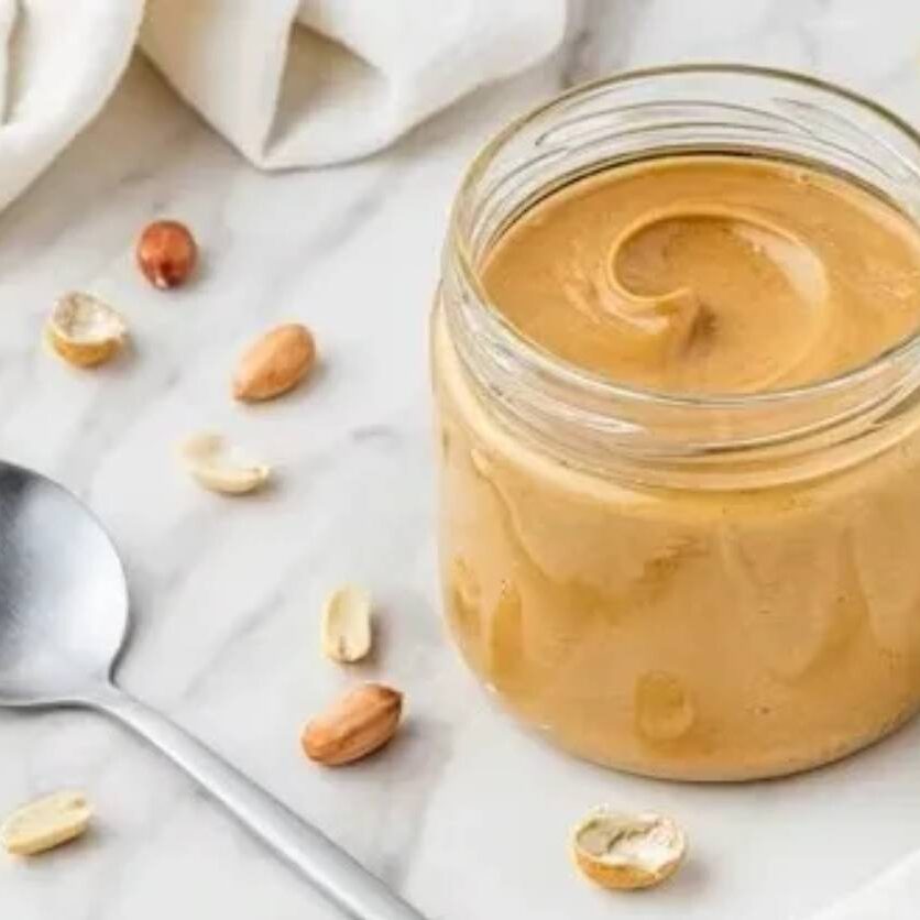 Glass jar of creamy peanut butter with peanuts
